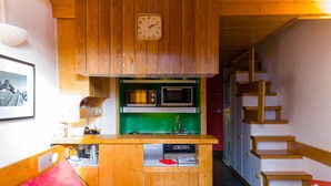 A compact kitchen with wooden cabinets, a microwave, and a sink. There is a red couch and a small table with a heater. A staircase is visible to the right. - Apartment Arc 1800 - 5 pers, Loft, Pets Allowed (Les Arcs 1800)