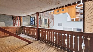 Una terraza de madera con barandilla, una escalera y vistas a un edificio con balcones.