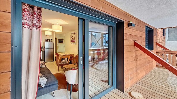 Una terraza de madera con un ventanal de vidrio que da a un comedor con mesa y sillas.