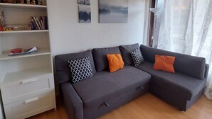A modern living room with a grey sectional sofa, white shelving with books and decorative items, and two framed artworks on the wall. - 22m² Studio for 4 near slopes (Les Deux Alpes)