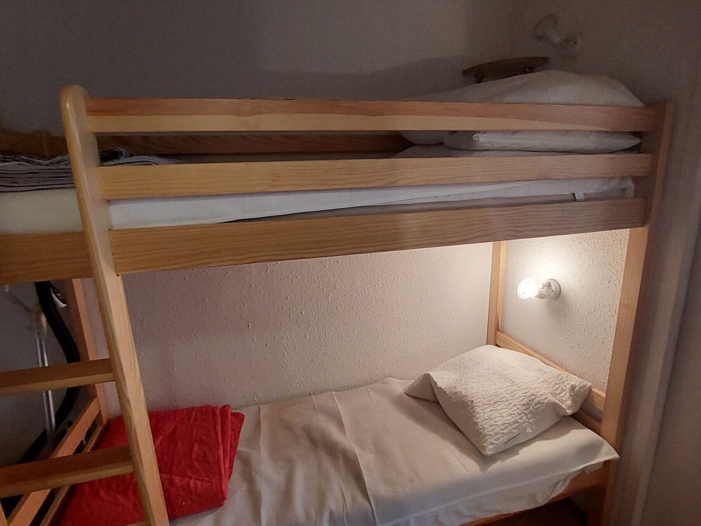 A bunk bed with a ladder, a red bag, and a white pillow.