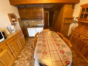 A kitchen with wooden cabinets, a tiled backsplash, a dining table with a patterned tablecloth, and a coffee maker. - Spacious apartment with south/west-facing balcony and WIFI connection (Châtel)