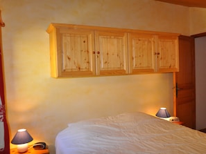 A bedroom with a bed, two bedside lamps, and wooden cabinets above the bed. - Spacious apartment with south/west-facing balcony and WIFI connection (Châtel)