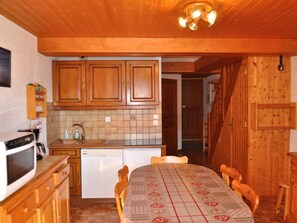 A kitchen with wooden cabinets, a microwave, a dishwasher, and a dining table with chairs. - Spacious apartment with south/west-facing balcony and WIFI connection (Châtel)