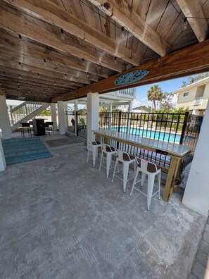 Un espace extérieur abrité comprenant une piscine, des tabourets de bar et un escalier menant à un niveau supérieur.