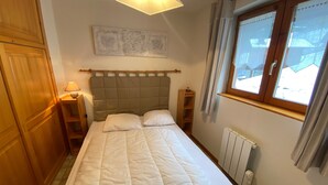 A bedroom with a bed, a nightstand, a lamp, a radiator, and a window with curtains. - Quiet apartment near the center with balcony and garage in Châtel (Châtel)