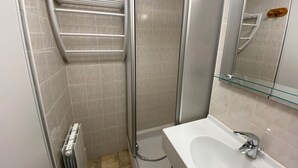 A bathroom with a glass shower enclosure, a white sink with a chrome faucet, and a glass shelf above the sink. - Quiet apartment near the center with balcony and garage in Châtel (Châtel)