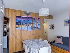 A cozy room with a wooden wall, a dining table with chairs, a sofa, and a hanging light fixture. - Cozy apartment for 5, close to slopes and shops (La Toussuire)