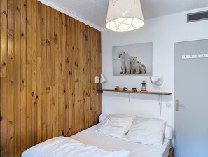 A bedroom with a wooden panel wall, a bed with white bedding, a ceiling lamp, a shelf with toys, and a polar bear picture on the wall. - Cozy apartment for 5, close to slopes and shops (La Toussuire)