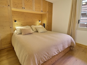 A bedroom with a wooden headboard, a bed with a beige bedspread, two pillows, and a nightstand with a lamp. - Stunning 4-room apartment, ski-in/ski-out, renovated, 6-7 pers., south (Méribel)