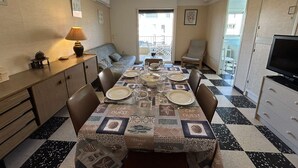 Un coin repas avec une table dressée pour quatre personnes, un ventilateur de plafond et une vue sur l’extérieur.