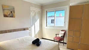 Une chambre à coucher avec un lit, une chaise, une armoire, un tableau et une fenêtre donnant sur un beau paysage.