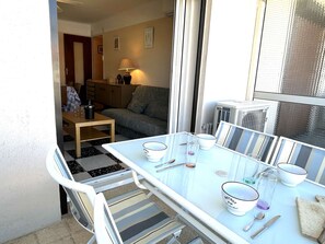 Un coin repas avec une table en verre, des chaises et des bols blancs. On aperçoit un canapé et une lampe au fond.