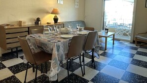 Un coin repas avec un sol à carreaux, une table mise avec des assiettes, des verres et une carafe, et une lampe sur la table.