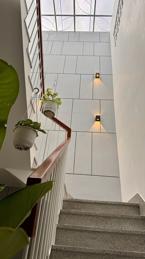 Un escalier aux murs blancs, deux appliques murales et des jardinières suspendues ornées de plantes vertes.