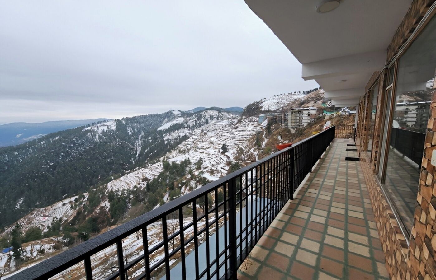 A balcony with a view of snow-covered mountains and a distant cityscape.
