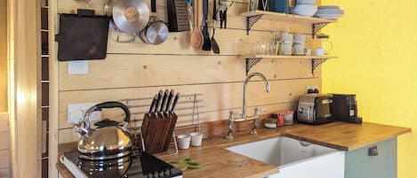 Una cocina con encimera de madera, un lavamanos, un hervidor, una cafetera y varios utensilios y utensilios de cocina colgados en la pared.