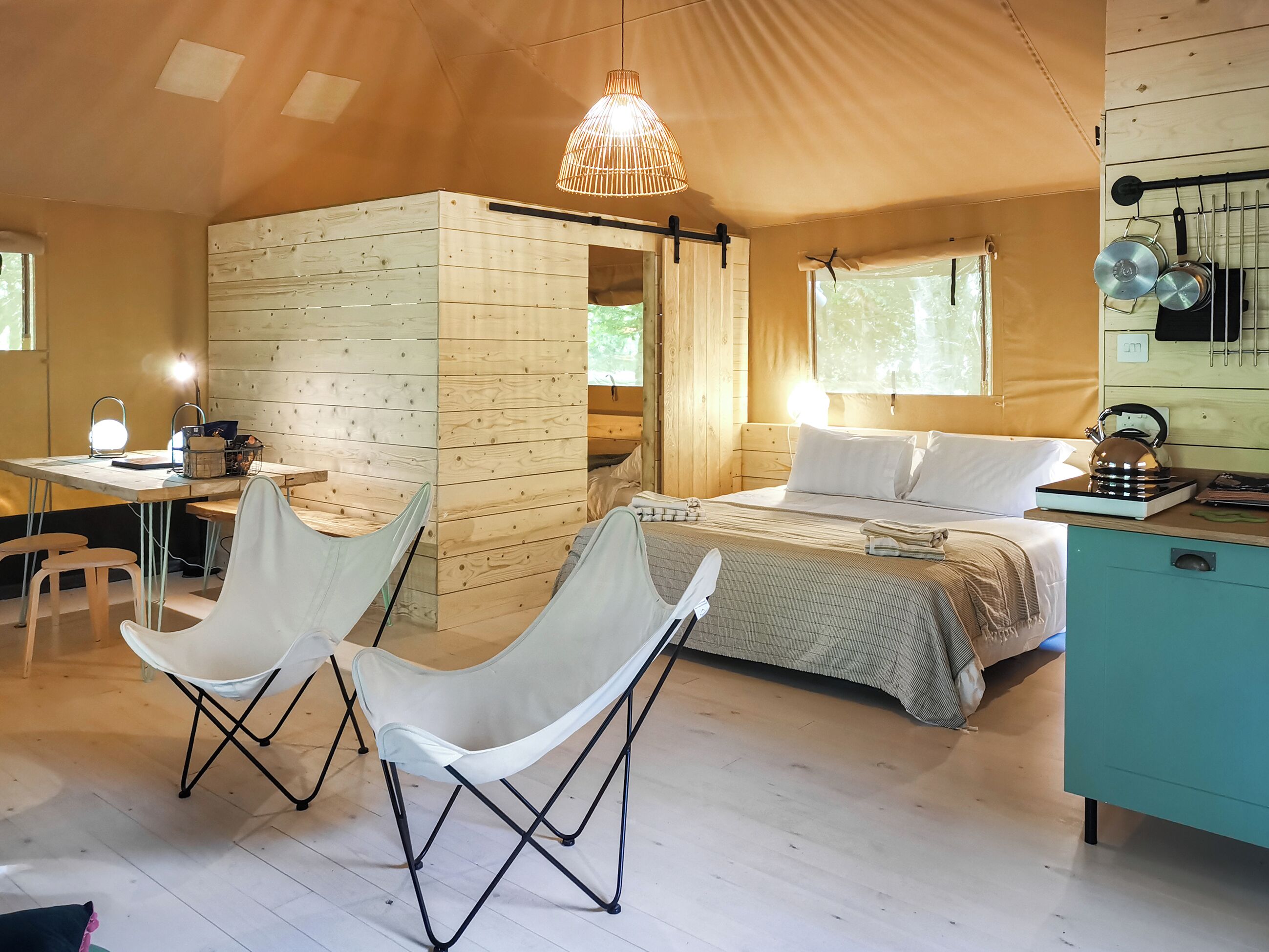 A cozy room with a bed, two chairs, a desk, and a hanging light fixture.