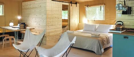 A cozy room with a bed, two chairs, a desk, and a hanging light fixture.