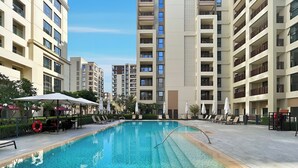A swimming pool surrounded by modern apartment buildings with balconies, sun loungers, and umbrellas. - 1BR Creek Beach Access (Dubai)