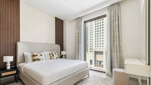 A modern hotel room with a large bed, a desk, and a view of a high-rise building. - 1BR Creek Beach Access (Dubai)