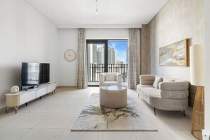 A modern living room with a flat-screen TV, a round coffee table, a sofa, and a large window offering a city view. - 1BR Creek Beach Access (Dubai)