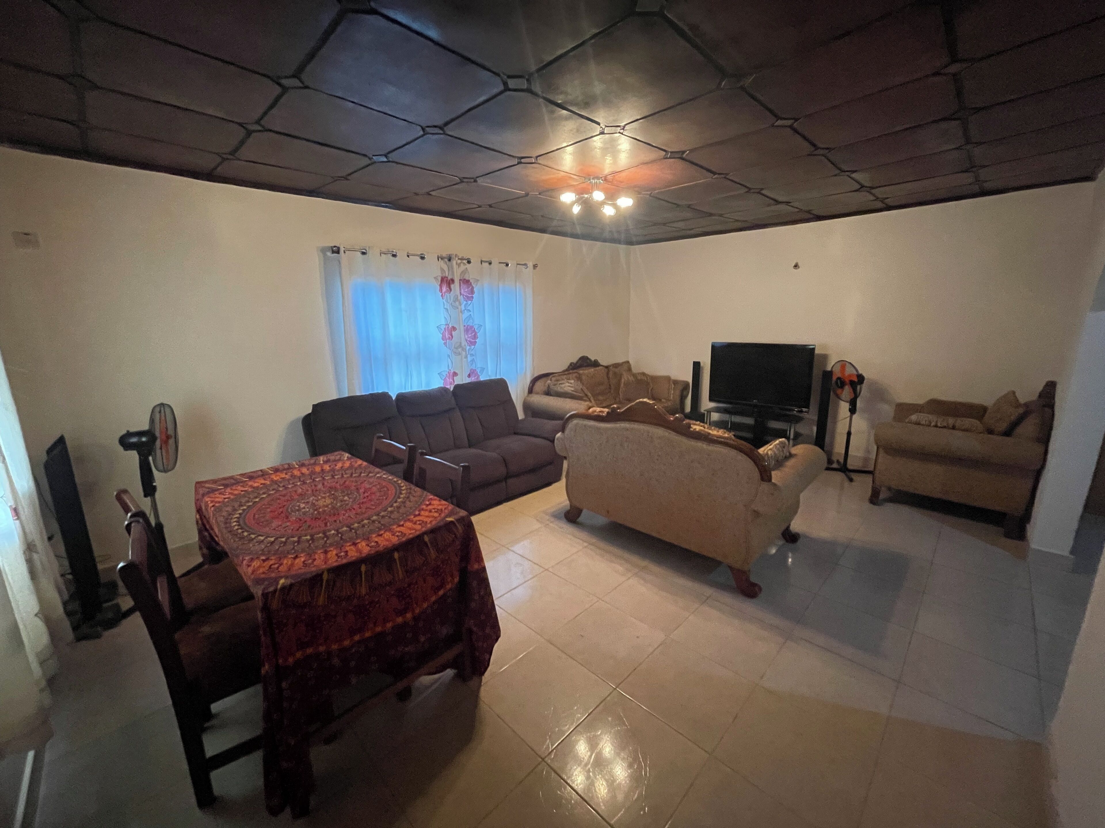 A living room with a sofa, a television, a coffee table, and a patterned tablecloth.