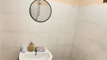 Un baño con lavamanos blanco, un espejo y artículos de aseo en la encimera.