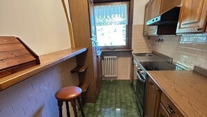 A narrow kitchen with wooden cabinets, a green tiled floor, and a window with a view of the outside.