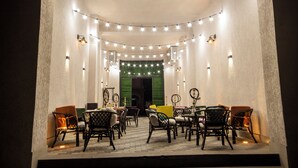An outdoor dining area with string lights, wicker chairs, and a green door in the background. - Kinor David Glatt Kosher Hotel  (Tbilisi)