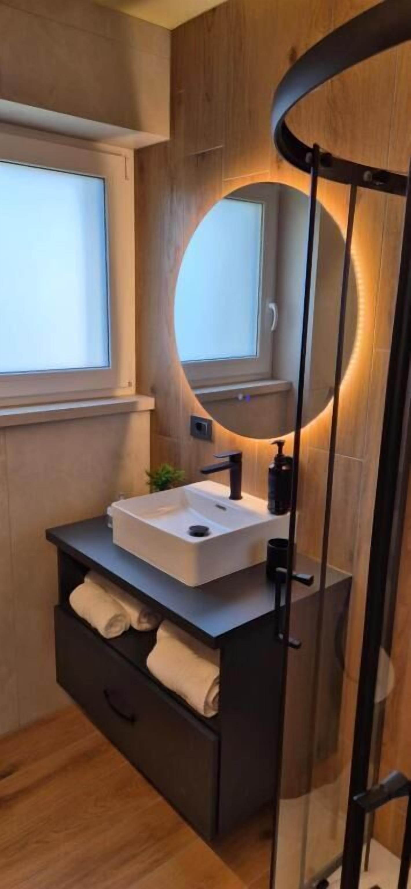 A modern bathroom with a wooden vanity, a round mirror, and a built-in sink.