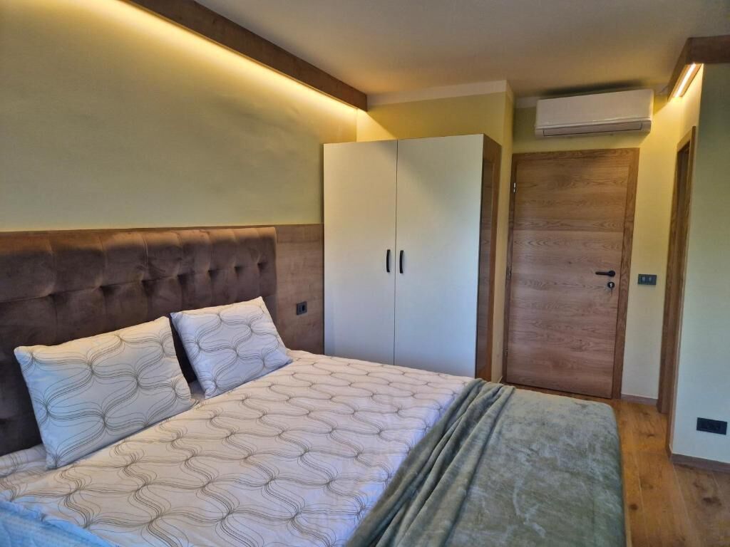 A bedroom with a tufted headboard, a bed with patterned bedding, a wardrobe, and a wooden door.