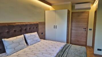 A bedroom with a tufted headboard, a bed with patterned bedding, a wardrobe, and a wooden door.