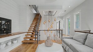 A modern interior with a staircase, a flat-screen TV, a round white ottoman, and a grey sofa. - Luxurious 7-Bedroom with Private Pool, Enchanting Courtyard and Game Room (Rosemary Beach)