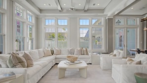 A spacious living room with a white sofa set, a coffee table, and large windows offering views of the outside. - Luxurious 7-Bedroom with Private Pool, Enchanting Courtyard and Game Room (Rosemary Beach)