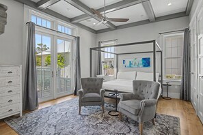 Une chambre à coucher avec un lit à baldaquin, deux fauteuils, une petite table et une grande fenêtre avec des rideaux.
