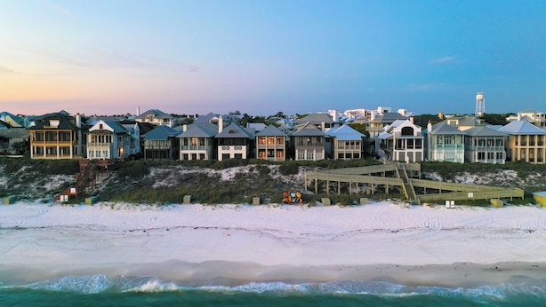 A beachfront property with multiple houses, a wooden boardwalk, and a water tower in the background. - Luxurious 7-Bedroom with Private Pool, Enchanting Courtyard and Game Room (Rosemary Beach)