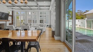 A spacious living area with a wooden dining table, white sofas, and a large sliding glass door leading to a pool. - Luxurious 7-Bedroom with Private Pool, Enchanting Courtyard and Game Room (Rosemary Beach)
