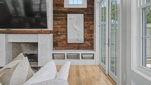 A living room with a fireplace, a mounted TV, and a large window with a view. - Luxurious 7-Bedroom with Private Pool, Enchanting Courtyard and Game Room (Rosemary Beach)