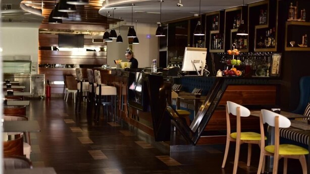 A modern bar area with a wooden floor, bar stools, and a counter with a digital display. - Tirana Room Rentals • Single Bed • Free Wi-Fi • Private Bathroom • TV (Tirana)