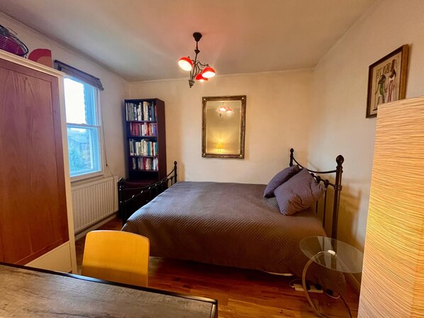 Une chambre à coucher avec un lit, une bibliothèque, une fenêtre, un miroir et une lampe.