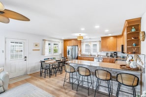 A modern kitchen with wooden cabinets, a central island with bar stools, and a dining area with a table and chairs.