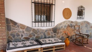 A stone wall, a wooden bench with patterned cushions, a rustic chair, and a woven wall hanging. - Rural house 'Sombrerocordobe' with private pool, jacuzzi, and air conditioning (Cordoba)