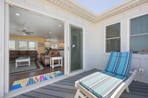 Un patio couvert avec un fauteuil de relaxation, une porte-fenêtre coulissante donnant sur un espace de vie et un ventilateur de plafond.