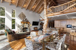 A spacious living area with a stone fireplace, wooden furniture, and a large window overlooking greenery.