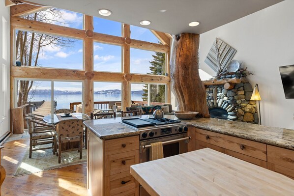 Cocina amplia con ventanas grandes, chimenea de piedra y vistas a un lago.