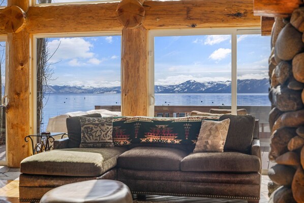 Una cabaña acogedora con un amplio ventanal con vistas a un lago y montañas.