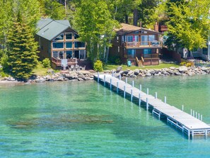 Une propriété au bord du lac, dotée d’un quai s’avançant dans l’eau, d’une grande maison avec plusieurs terrasses et d’un bâtiment plus petit situé à côté.