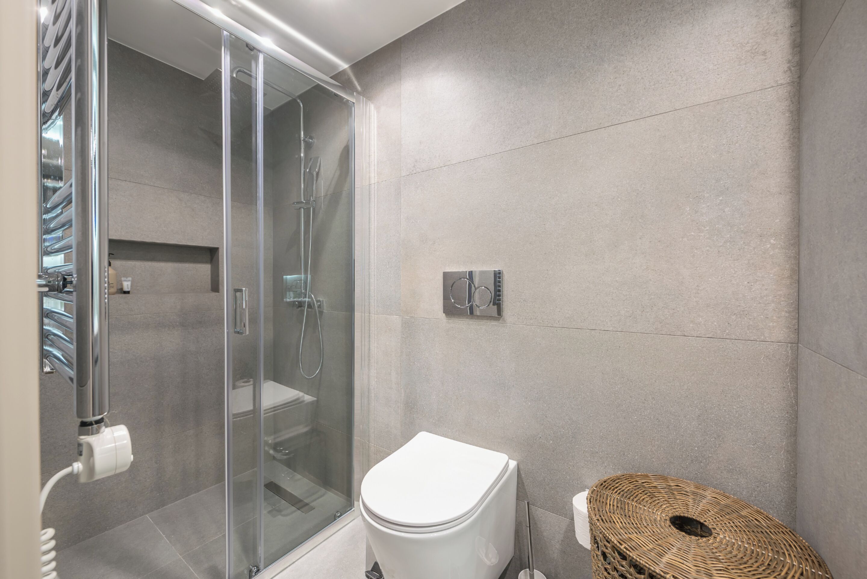 Ein modernes Badezimmer mit einer gläsernen Duschkabine, einer weißen Toilette und einem Korbstuhl.