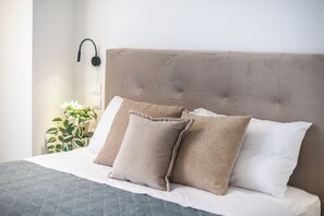 Een net opgemaakt bed met een grijze quilt, twee beige kussens en een wit kussen.